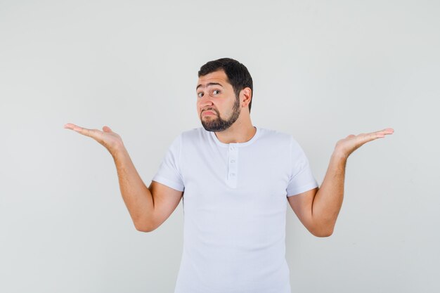 Young man showing helpless gesture in t-shirt and looking troubled. front view.