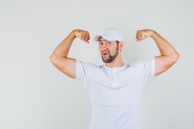 Бесплатное фото Молодой человек показывает мышцы рук в футболке, кепке и отлично выглядит, вид спереди.