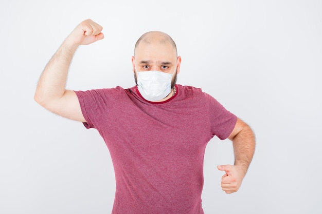 Young man showing his arm muscles in pink t-shirt,mask and looking powerful , front view.