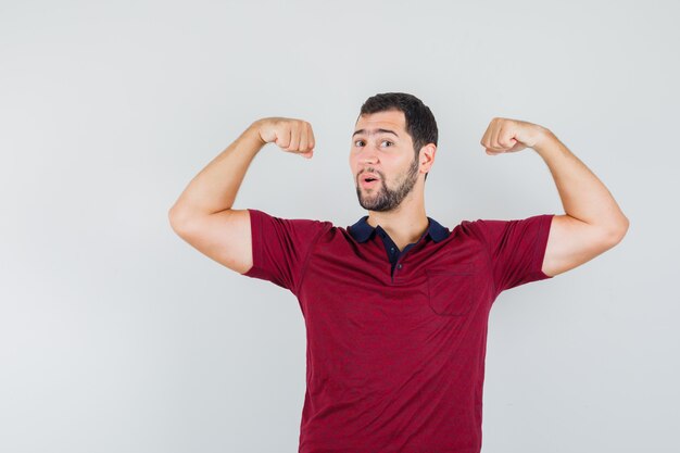 Young man showing his arm muscles in red t-shirt and looking satisfied. front view.