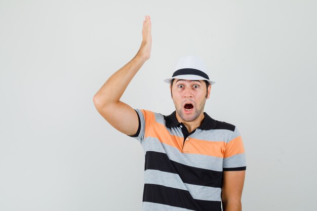 Young man showing his feelings in t-shirt,hat and looking surprised. front view.