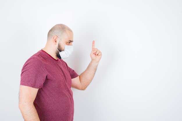 Молодой человек показывает палец как предупреждение в розовой футболке, маске. место для текста