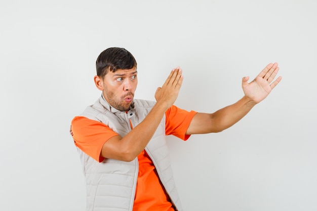 Young man showing karate chop gesture in t-shirt, jacket and looking powerful