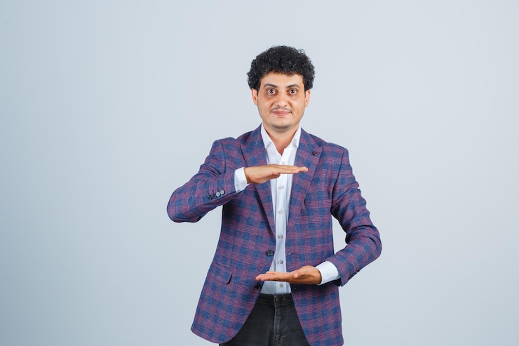 मुफ़्त फोटो शर्ट, जैकेट पहने एक युवक बड़े आकार का संकेत दिखा रहा है और आत्मविश्वास से देख रहा है। सामने का दृश्य।
