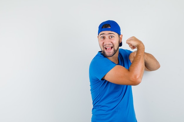 Young man showing muscles of arm in blue t-shirt and cap and looking powerful