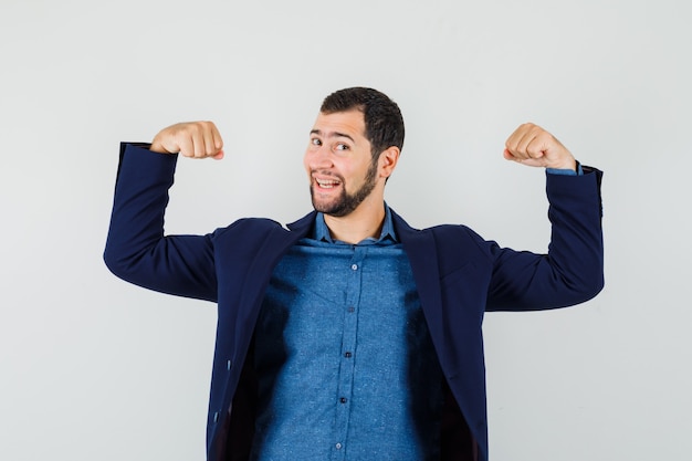 Young man showing muscles of arms in shirt, jacket and looking cheerful.