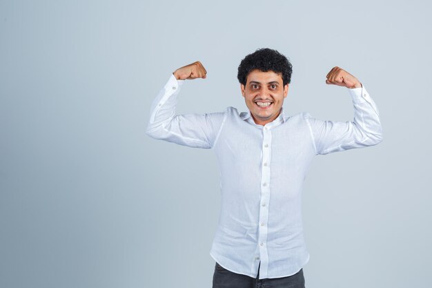 Young man showing muscles of arms in white shirt and looking powerful , front view.