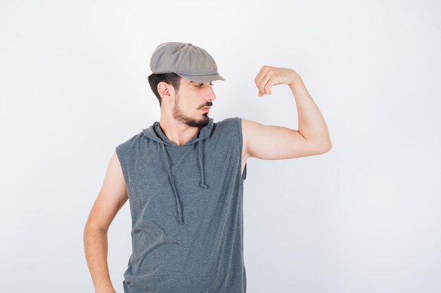 Young man showing muscles in gray t-shirt and cap and looking serious