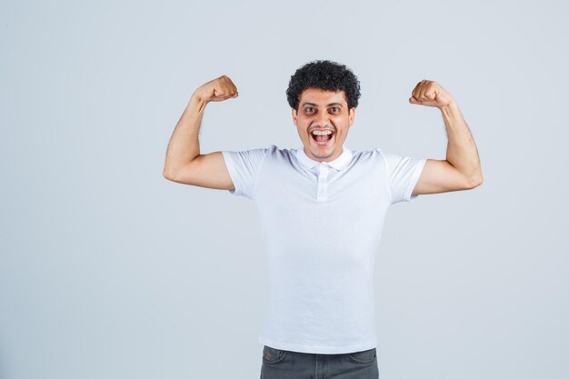 Young man showing muscles in white t-shirt and jeans and looking powerful. front view.