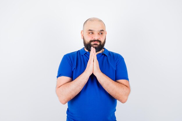 Young man showing namaste gesture in blue shirt and looking thankful , front view.