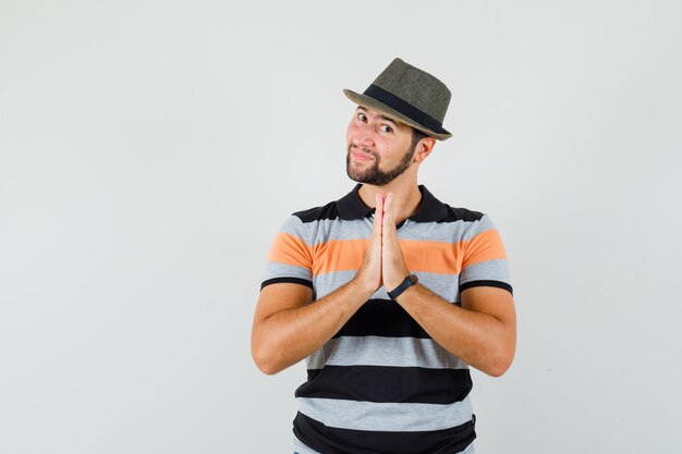 Young man showing namaste gesture in t-shirt, hat and looking grateful