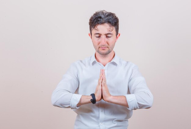 Young man showing namaste gesture in white shirt and looking calm