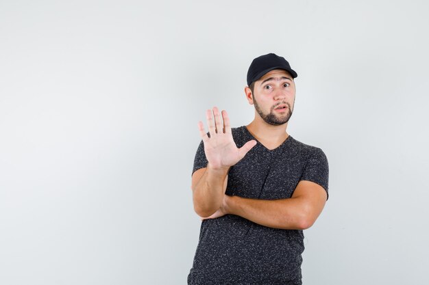 Young man showing no gesture in t-shirt and cap and looking scared