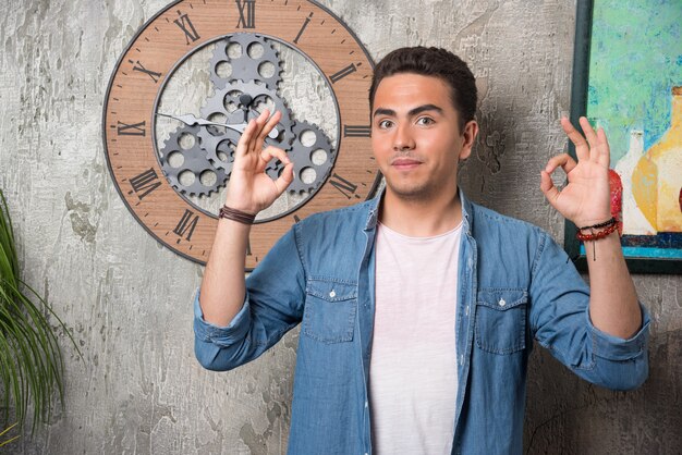 Young man showing ok gesture and posing on marble background. High quality photo