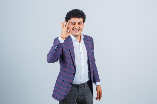 Young man showing ok gesture in shirt, jacket, pants and looking confident , front view.