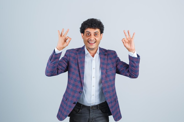 Free photo young man showing ok gesture in shirt, jacket, pants and looking confident , front view.