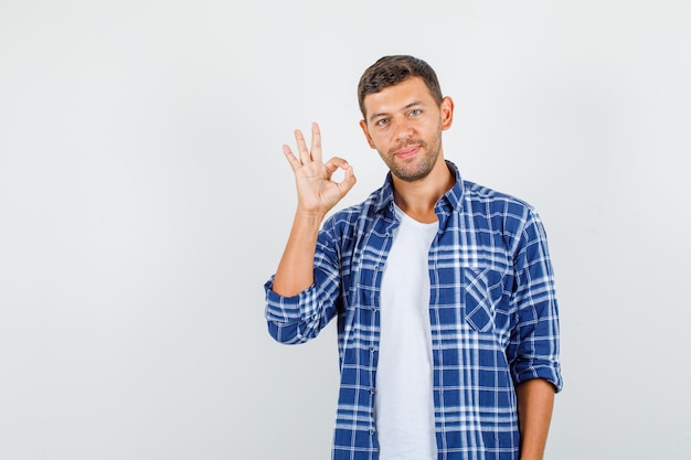 Young man showing ok gesture in shirt and looking pleased. front view.