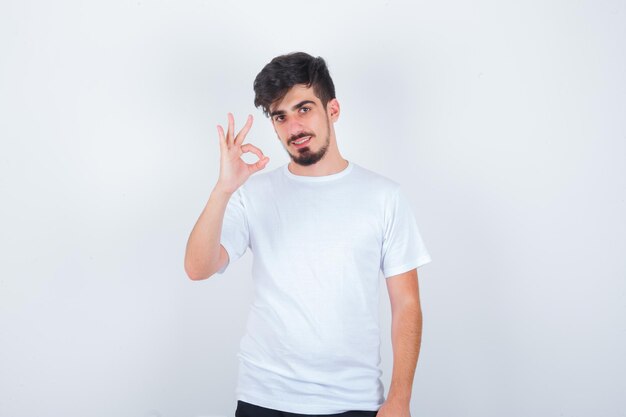Молодой человек показывает жест в белой футболке и выглядит уверенно