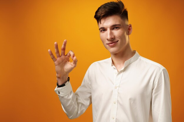 Young man showing ok sign against yellow background