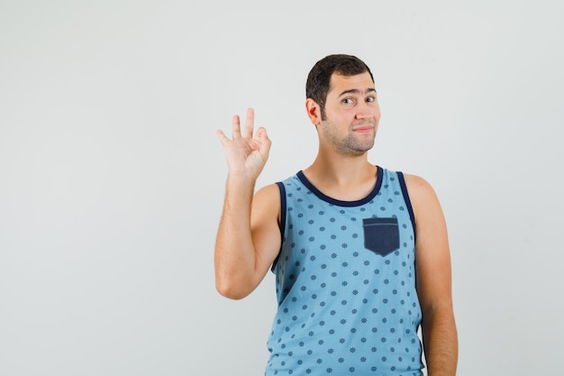 Young man showing ok sign in blue singlet and looking jolly. front view.