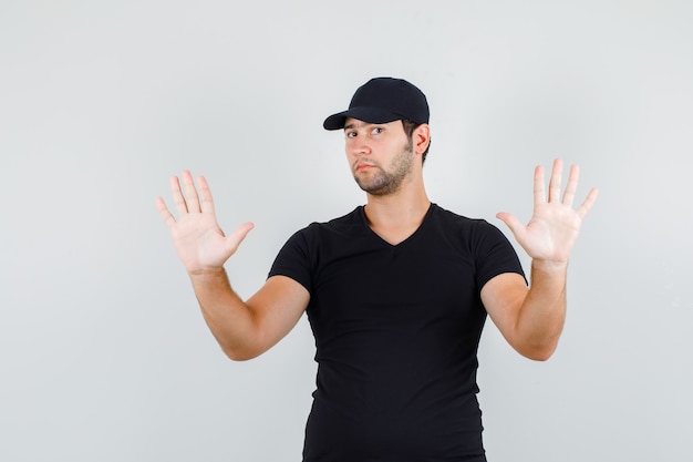 Young man showing raised palms in black t-shirt