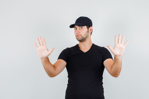 Молодой человек показывает поднятые ладони в черной футболке