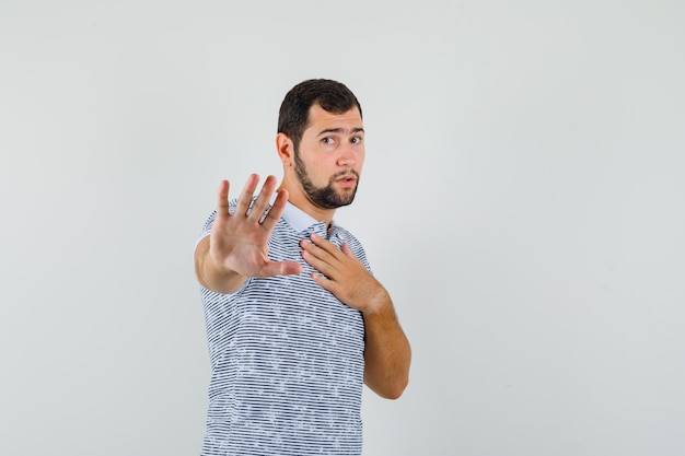 Young man showing refusal gesture by pointing at himself in t-shirt and looking serious , front view.