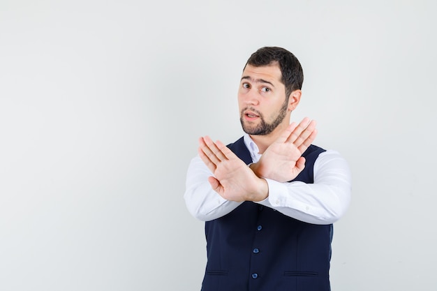 Young man showing refusal gesture in shirt and vest and looking serious