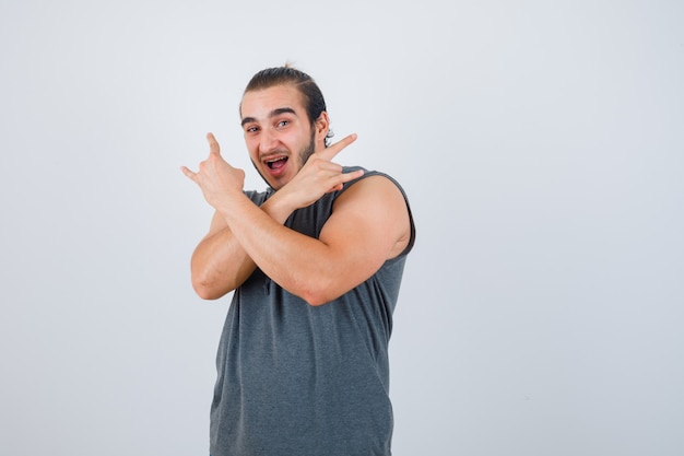 Young man showing rock gesture in sleeveless hoodie and looking happy , front view.