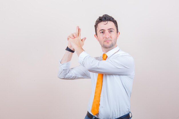 Young man showing shooting gesture in white shirt, tie and looking confident