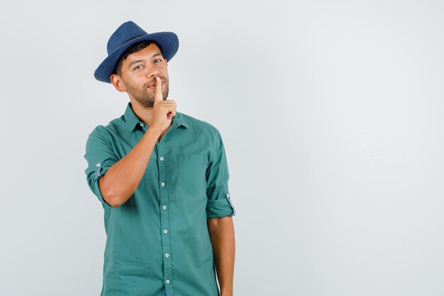 Young man showing silence gesture and smiling in shirt