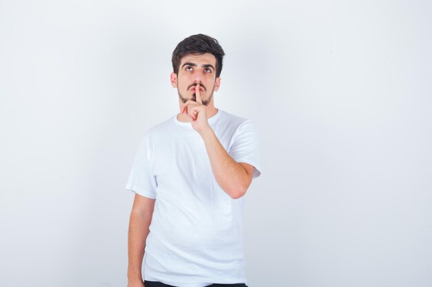 Young man showing silence gesture in t-shirt and looking confident