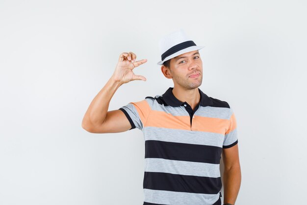 Young man showing small size sign in t-shirt and hat and looking cute