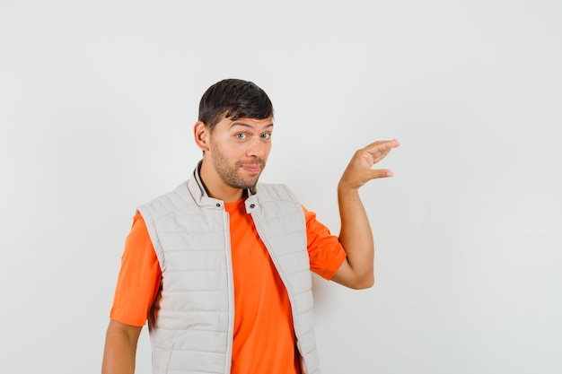 Young man showing small size sign in t-shirt, jacket and looking cheery