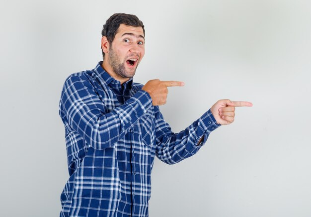 young man showing something away in checked shirt and looking cheerful