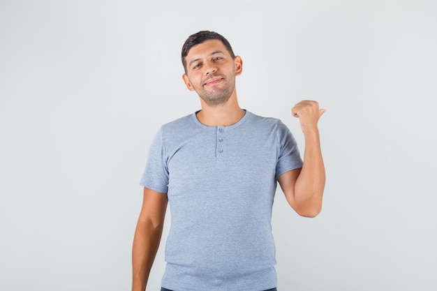 Young man showing something behind in grey t-shirt and looking glad