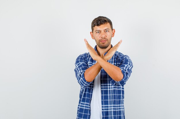 Young man showing stop gesture in shirt and looking confident. front view.