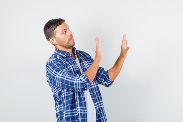 Young man showing stop gesture while looking to side in shirt and looking scared. front view.