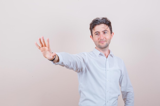 Young man showing stop gesture in white shirt and looking cheery