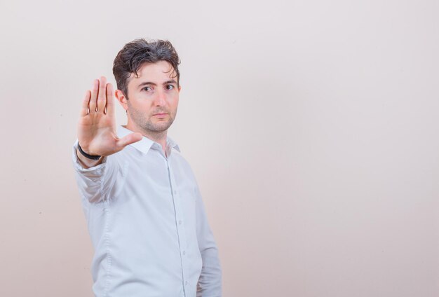 Free photo young man showing stop gesture in white shirt and looking confident