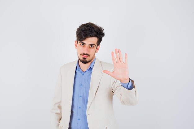 Young man showing stop sign in blue t-shirt and white suit jacket and looking serious