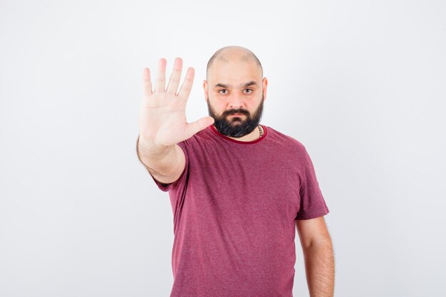 Young man showing stop sign in pink t-shirt and looking serious , front view.