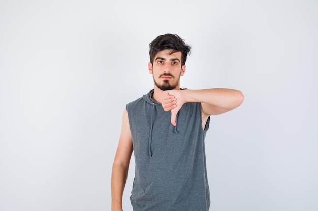 Young man showing thumb down in gray t-shirt and looking serious