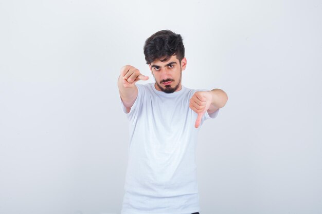 親指を下に見せて、白いTシャツで正面を指して、自信を持って見える若い男