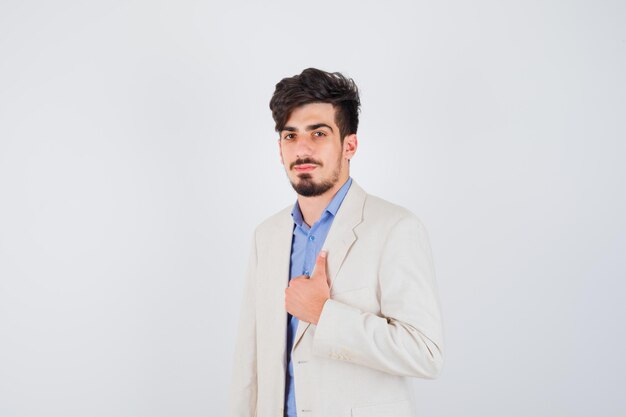 Young man showing thumb up in blue t-shirt and white suit jacket and looking serious