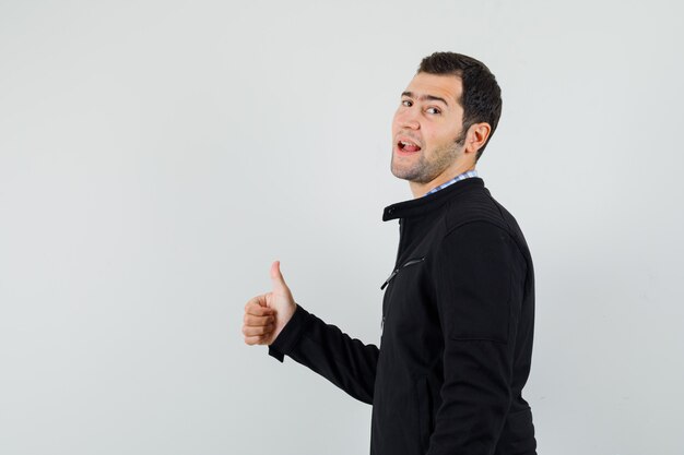 Young man showing thumb up in shirt, jacket and looking confident .