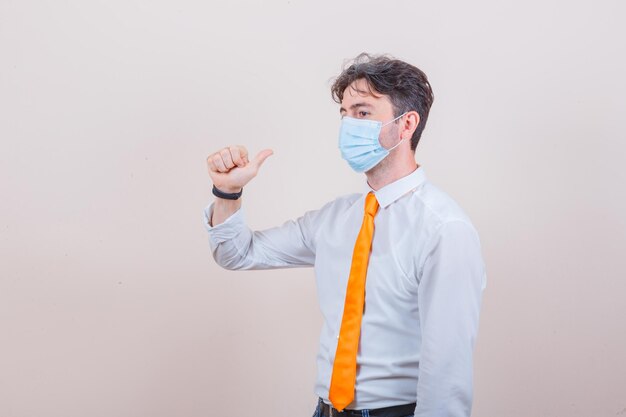 Young man showing thumb up in shirt, tie and mask