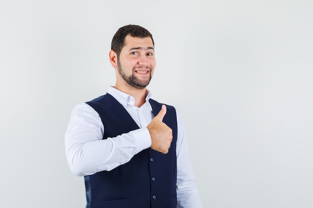 Young man showing thumb up in shirt and vest and looking jolly