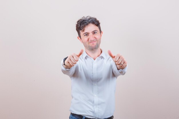 Young man showing thumbs up in white shirt, jeans and looking pleased