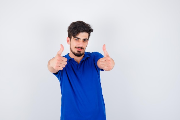 Young man showing thumbs up with both hands in blue t-shirt and looking optimistic